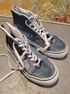 A brand new pair of sparkly blue hi-top sneakers with white laces sits on the floor with the shoelaces untied.