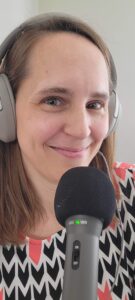 Sara smiles at the camera, wearing headphones and a fun patterned dress with a professional microphone in front of her and headphones over her ears.