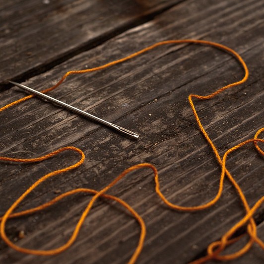 Golden thread with needle nearby on wooden table