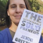 Sara stands outside smiling as she proudly holds up her copy of Jenni Gritter's "The Sustainable Solopreneur"