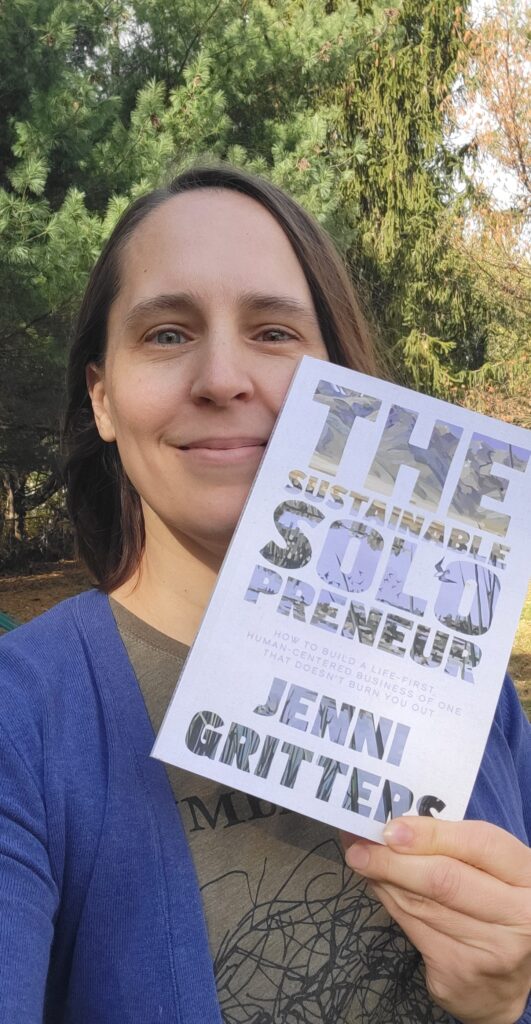 Sara stands outside smiling as she proudly holds up her copy of Jenni Gritter's "The Sustainable Solopreneur"