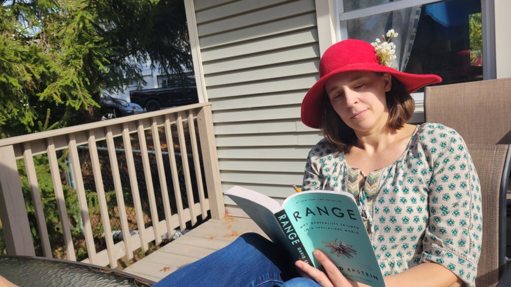 Sara sits on her deck reading the book with a contemplative look on her face as the sun shines down.